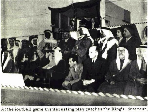 King Saud—may God have mercy on him—watching a football match at the Sports Center in Dhahran, accompanied by Sheikh Jamal al‑Husseini, in 1954.