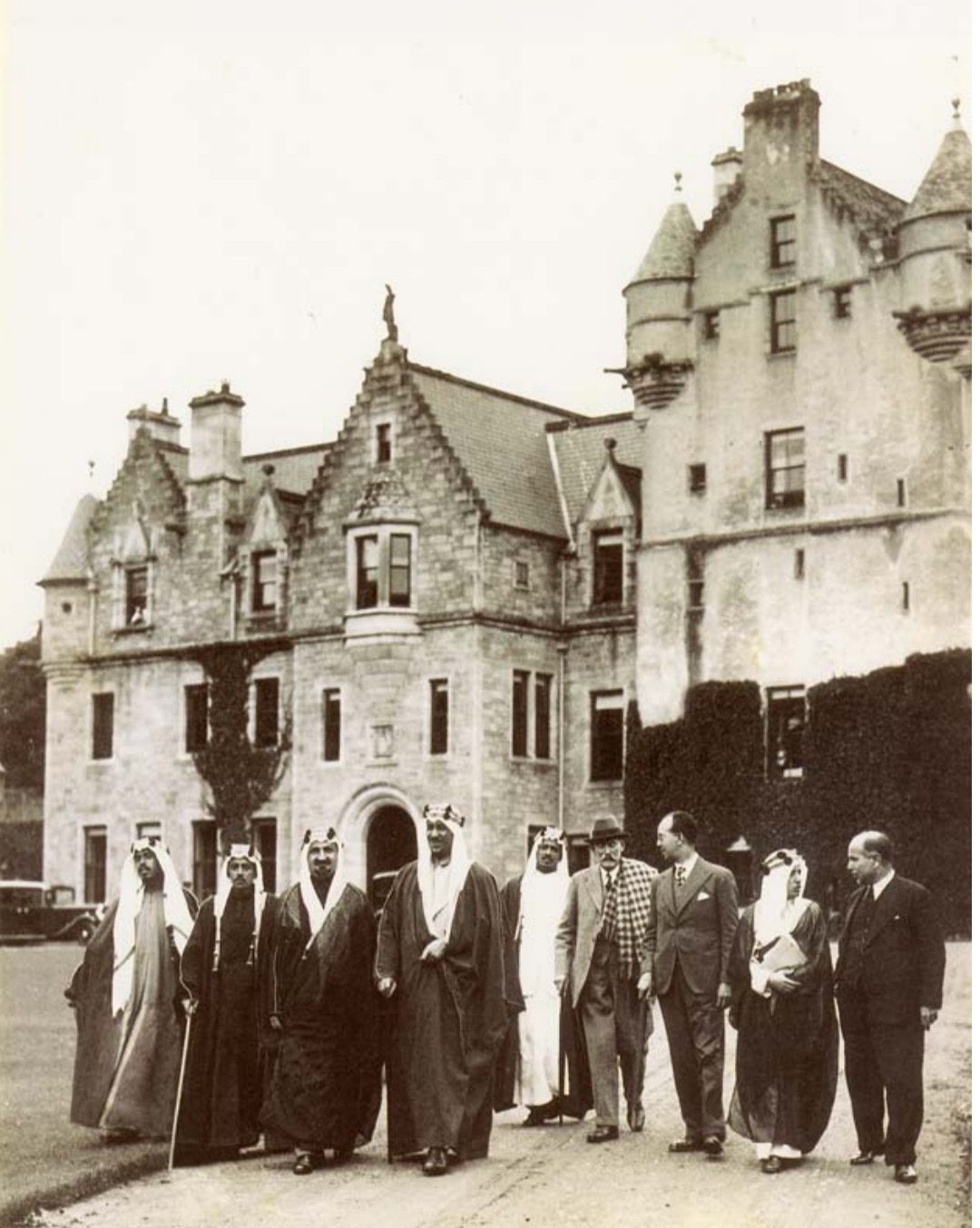 The photograph was taken on 8 July 1937 at Udny Castle in Scotland, showing Crown Prince Saud (later King Saud) together with Sheikh Yusuf Yassin, Dr. Medhat Sheikh Al‑Ard, and his escorts Abdulaziz Al‑Rifai and Saleh Al‑Ali Al‑Salem