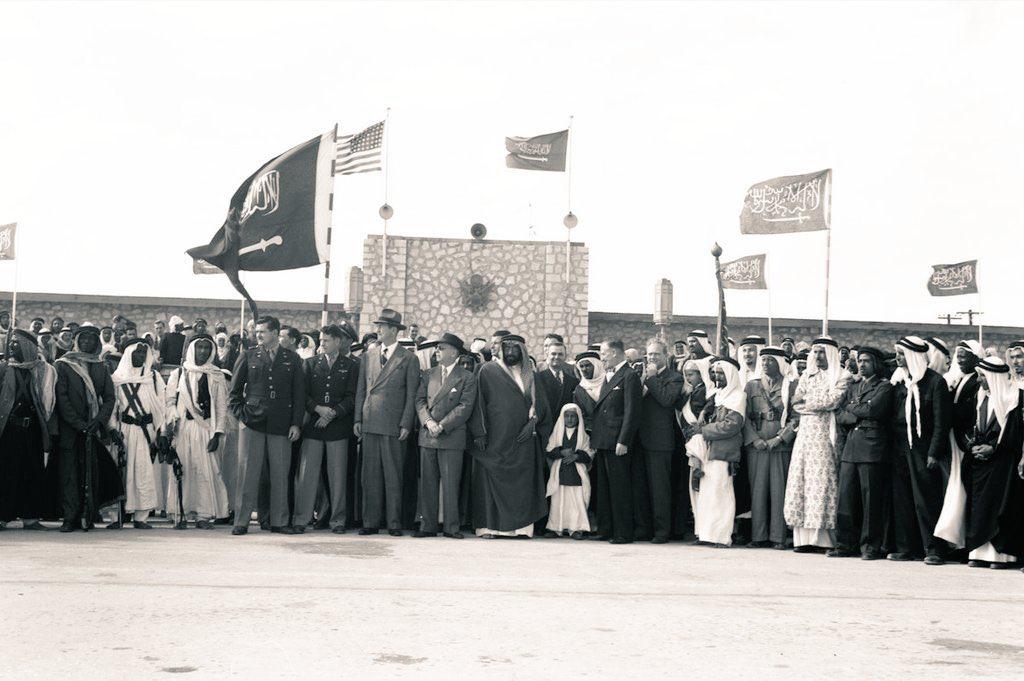 Prince Saud bin Abdullah bin Jiluwi standing among senior dignitaries to receive King Saud—may God have mercy on him—, with the two children beside him identified as Prince Saad Al‑Faisal and Prince Khalid Al‑Faisal.